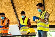 Group Of Engineering Team Wear Protective Face Masks Safety For Coronavirus Disease 2019 (COVID-19) Meeting To Plan For New Project  Measuring Layout Of Building Blueprints In Construction Site.