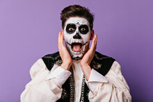 Shocked Brown-eyed Man Screaming On Purple Background. Handsome Male Model In Zombie Costume Expressing Amazement In Halloween.