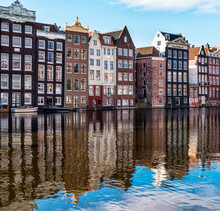 Traditional Buildings Along The Damrak Reflected In The Canal, Amsterdam, The Netherlands