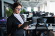 © Михаил Решетников - Serious business woman in a suit answers the customer's call on the headset. Female manager takes notes while talking with a client. Administrator at work in the office.