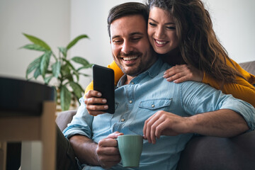 Wall Mural - Cheerful couple using mobile phone at home stock photo