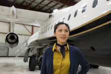 Portrait Female Flight Attendant By Airplane In Hangar