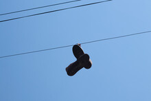 Old Dirty Sneakers Hang On A Wire On A Pole Against A Blue Sky