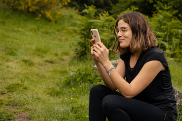 Young woman sat using her mobile phone while resting after a hike in the nature