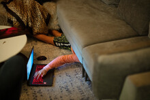 A 12-year Old Boy Hides Under Couch While Using A Laptop Computer
