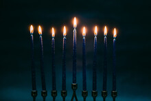 Burning Blue Candles On A Jewish Menorah At Hanukkah With A Dreidel On A Dark Blue Background