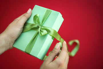 Girl holds a gift box and unties the bow. a girl opens a gift box. Gift box on a red background. Girl unties the tape from the box.
