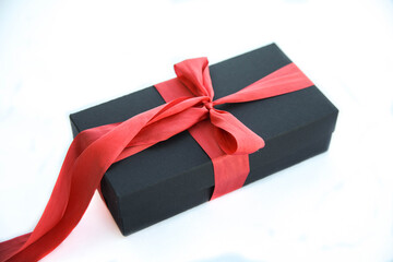 Girl holds a gift box and unties the bow. a girl opens a gift box. Gift box on a red background. Girl unties the tape from the box.
