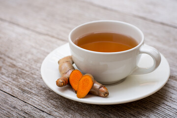 Wall Mural - Closeup cup of hot Turmeric tea with tumeric root isolated on wood table background . 