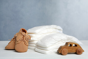 Wall Mural - Baby diapers, child's shoes and toy car on white wooden table against grey background