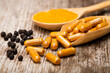 Curcuma capsules and Curcumin powderin wooden spoon and black peppercorns isolated on rustic wood table background. Health benefits and antioxidant food concept.