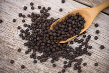 Black Pepper Seeds Or Peppercorns ( Dried Seeds Of Piper Nigrum) In Wooden Spoon Isolated On Wood Table Background. Top View. Flat Lay.