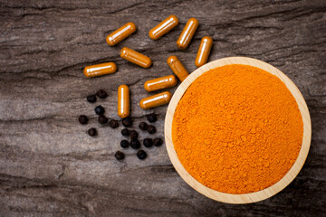 Turmeric ground or tumeric powder in wooden bowl with curcuma capsule and black pepper ( peppercorns or piper nigrum )  isolated on wood table background. Top view. Flat lay.