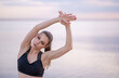 © kalinichenkod - young girl in fitness clothes by the sea performs exercises