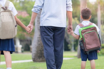 Asian young father holding hand his son and daughter walking to school in the morning
