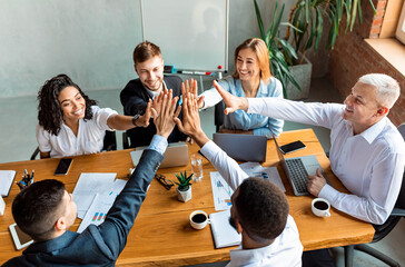 Business Team Giving High-Five Sitting At Table In Modern Office