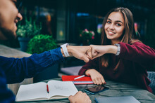Cheerful Brunette Woman Looking At Camera Bumping Fist With Male Colleague Making Agreement Cooperating On Homework, Cropped Image Of Positive Hipster Friends Greeting On Meeting In Cafe Terrace