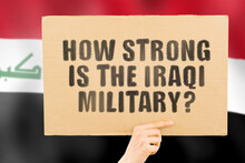 The Question " How Strong Is The Iraqi Military? " On A Banner In Men's Hand With Blurred Iraqi Flag On The Background. Violation. Conflict. War. Pressure. Combat. Crime Against Humanity