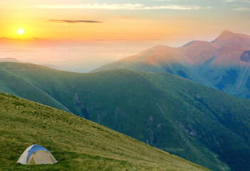 Wall Mural - Tourist tent located in summer mountains at sunset. Hiking camp in evening nature. Travel and get away concept.