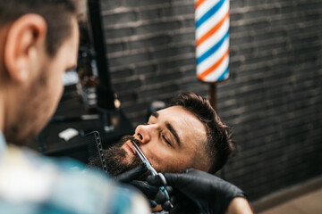 Young good looking man visiting barber shop. Trendy and stylish beard styling and cut.