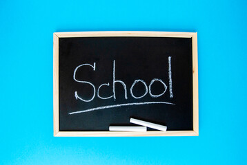 The word school is written in chalk on a black chalkboard in a frame and two pieces of chalk lie. Chalk board is on a blue background