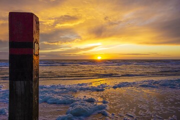 Wall Mural - beautiful shot of a sunset in dutch island of texel beach with beach pole and foam on the sand