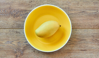 Wall Mural - pale yellow mango on a bright yellow plate on a wooden tabletop