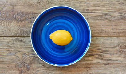 Wall Mural - bright yellow lemon on a blue plate on a wooden tabletop