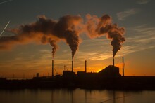 Low Angle Shot Of A Factory With Smoke And Steam Coming Out Of The Chimneys Captured At Sunset