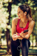 © chika_milan - Young attractive caucasian female runner taking a break after running and using smart phone.