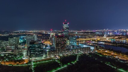 Poster - Aerial panoramic view over Vienna city with Donau City skyscrapers, historic buildings and a riverside promenade night timelapse in Austria. Illuminated skyline from Danube Tower viewpoint