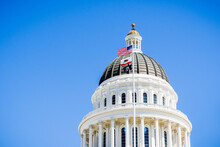The US And The California State Flag Waving In The Wind In Front Of The Dome Of The California State Capitol, Sacramento, California