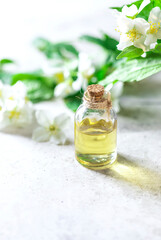 Wall Mural - Aromatic oil in glass bottle with fresh jasmine flowers on a light gray concrete background. Flower essential oil, osmetic oil perfume .