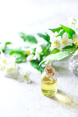 Wall Mural - Aromatic oil in glass bottle with fresh jasmine flowers on a light gray concrete background. Flower essential oil, osmetic oil perfume .