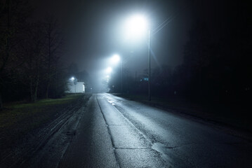 An empty old asphalt road in a fog at night. Street Lights close-up. Dark urban scene, cityscape. Riga, Latvia. Dangerous driving, speed, freedom, concept image