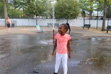 Young African American Girl Playing In City Park Sprinkler