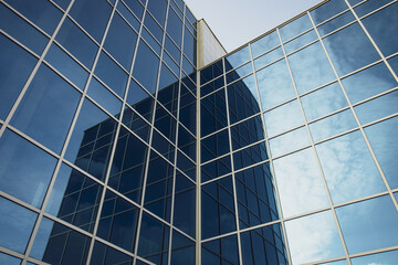 Modern office building with glass windows and blue sky. Dark blue texture of high-rise buildings. Abstract mirror wall background of skyscraper.