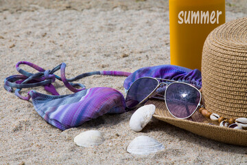 tanning lotion, sunglasses, hat and bikini on the beach