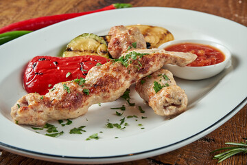 Appetizing rolls of Lyulya kebab - cooked from chicken minced meat in white plate with grilled vegetables. Wooden background