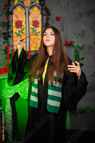Cuadros en Lienzo Young woman in a black cloak with a magic wand in her hands, standing against the backdrop of a medieval window