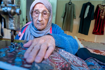 Wall Mural - Arabic muslim old woman using old sewing machine