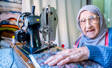 Wall Mural - Arabic muslim old woman using old sewing machine