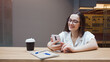 © Alexander - student girl is sitting at a table and using an app on her smartphone.