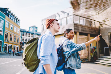 Multicultural male and female backpackers discussing showplaces while exploring touristic city, diverse man and woman in casual clothing walking and communicating during travel tour on vacations