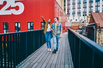 African American woman in trendy casual wear pointing on urban setting walking with her boyfriend on weekends, multiracial couple in love spending vacation together having trip and city tour