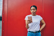 © BullRun - Young African American woman in casual wear read income message on mobile phone standing on red wall background, teen darks skinned blogger using 4G connection for chatting with followers online