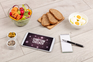 SYMPTOM CHECKER concept in tablet pc with healthy food around, top view