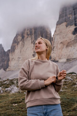 Wall Mural - Dolomites Alps. Italy. Happy blonde girl smiles on background of Tre Cime di Lavaredo mountains with peaks wrapped by grey clouds