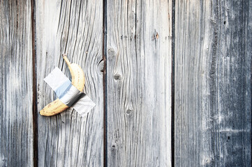 Yellow banana duct-taped to a weathered wooden wall - Concept of potassium and healthy lifestyle with seasonal fruit - Vitamins and vegan lifestyle for health people-Modern art and world trade concept