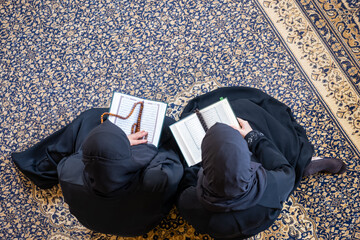 Muslim mother and her daughtersitting togther reading holy book